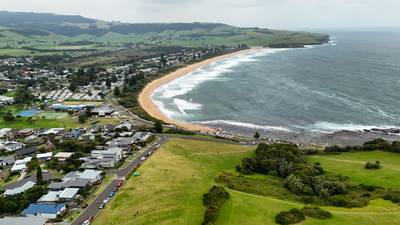 Panoramic aerial view of the long golden sands of Werri Beach with green hills and residential houses in the background.