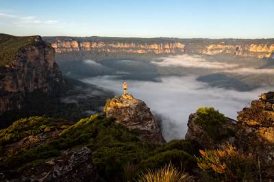 Hiker taking in magnificent views of mountains and valleys as the first light hits the sandstone escarpment cliffs