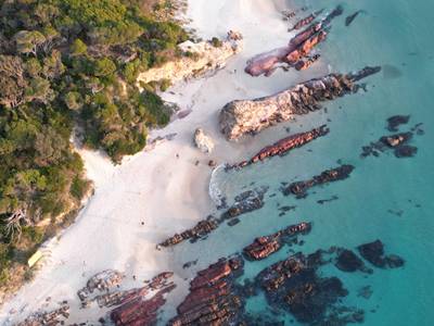 Aerial shot of rocks on the sandy beach with crystal clear water in Merimbula, Australia.