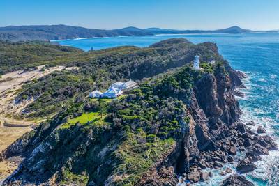 Aerial view of the historic Seal Rocks Lighthouse overlooking the rugged coastline, deep blue ocean and surrounding coastal landscape at…