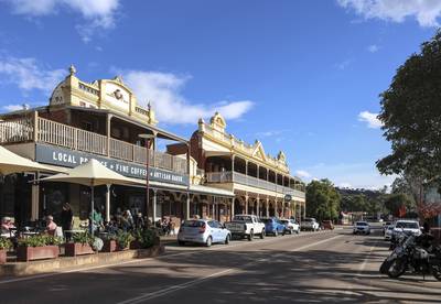 Street view, historic town. Featuring heritage colonial buildings, the local bakery, outdoor dining tables, parked cars. Copy space in sky