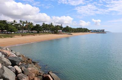 View of the beach lined with palm trees, the ocean and rocks at The Strand in Townsville, Queensland, Australia