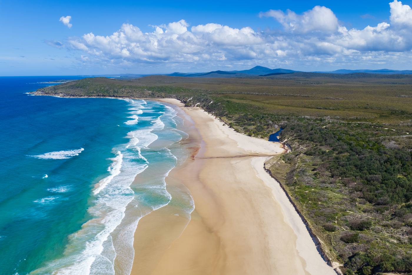 Aerial view of a long sandy beach and turquoise water at Angourie, near Yamba