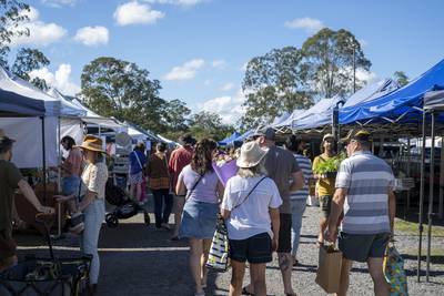 Shoppers walking between market stalls at a busy community farmers market.